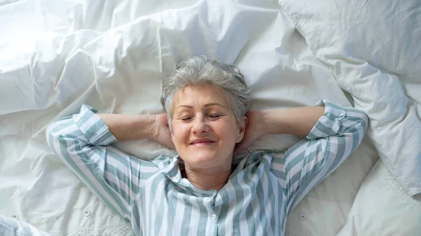 Horní pohled na šťastnou seniorku v posteli doma, oči zavřené. — Stock fotografie