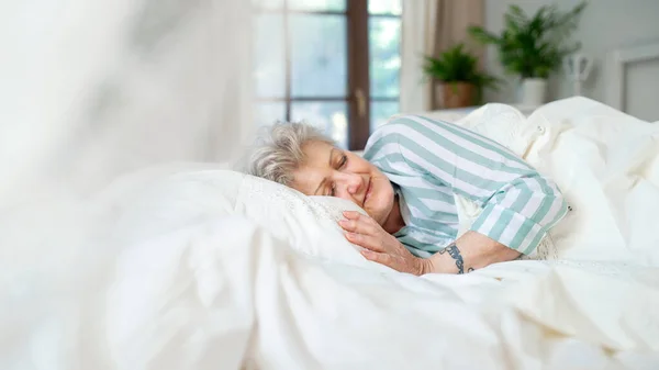 Ευτυχισμένη ηλικιωμένη γυναίκα στο κρεβάτι στο σπίτι, κοιμάται. — Φωτογραφία Αρχείου