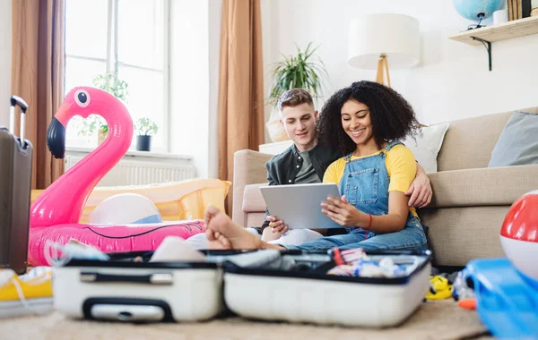 Joyeux jeune couple d'emballage pour des vacances d'été à la plage à la maison, en utilisant la tablette. — Photo