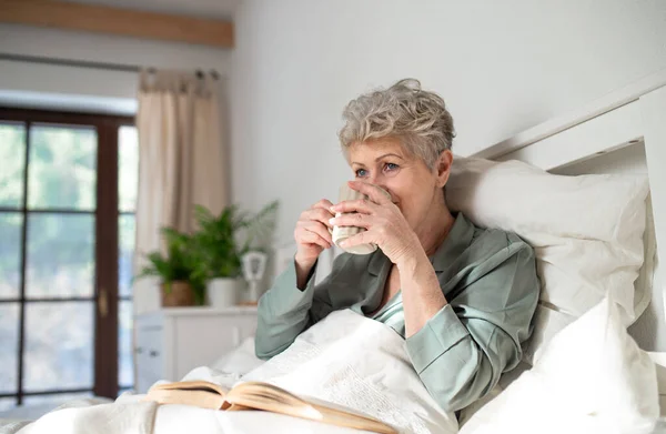 Mulher sênior feliz ler livro e beber café na cama em casa. — Fotografia de Stock