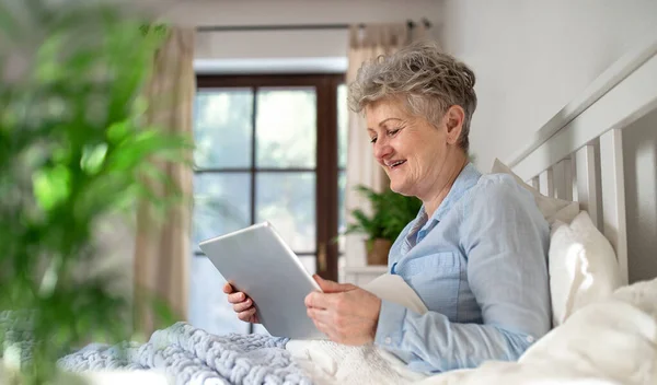 Mujer mayor feliz usando la tableta en la cama en casa. — Foto de Stock