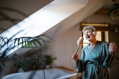 Evde kulaklık takıp şarkı söyleyen mutlu, son sınıf öğrencisi kadın, rahatla ve kendine dikkat et..