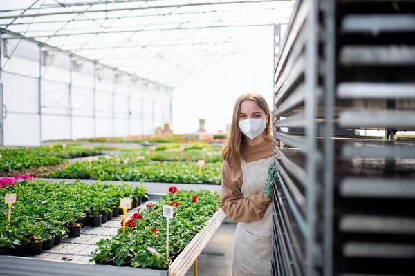 Mujer joven trabajando en invernadero en el centro de jardinería, concepto coronavirus. — Foto de Stock