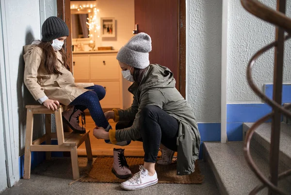 Мать с маленькой дочкой надевают туфли перед входной дверью, коронавирус. — стоковое фото