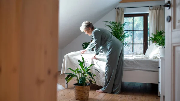 Mujer mayor en la cama en casa levantándose por la mañana, haciendo una cama. — Foto de Stock