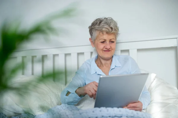 Heureuse femme âgée utilisant la tablette dans le lit à la maison. — Photo