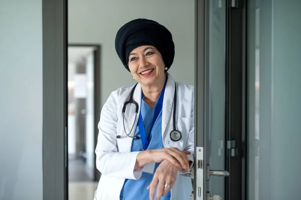 Portret starszej pani doktor stojącej w szpitalu, patrzącej w kamerę. — Zdjęcie stockowe