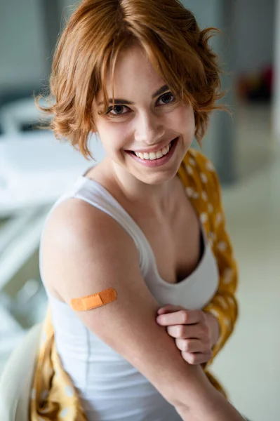 Femme heureuse avec du plâtre sur le bras après la vaccination à l'hôpital, regardant la caméra. — Photo