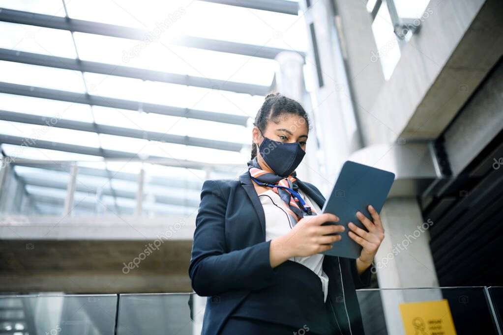 Young air hostess with tablet in airport lounge, coronavirus, travel and new normal.