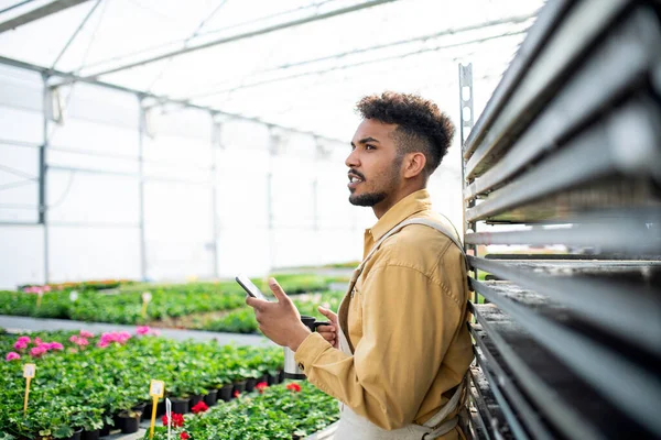 Joven afroamericano trabajando en invernadero, tomando un descanso para tomar café. — Foto de Stock