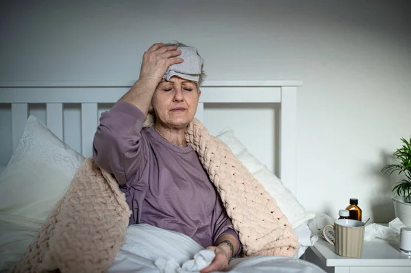 Mujer anciana enferma con dolor de cabeza en la cama en casa, dolor de cabeza y efectos secundarios de la vacunación. — Foto de Stock