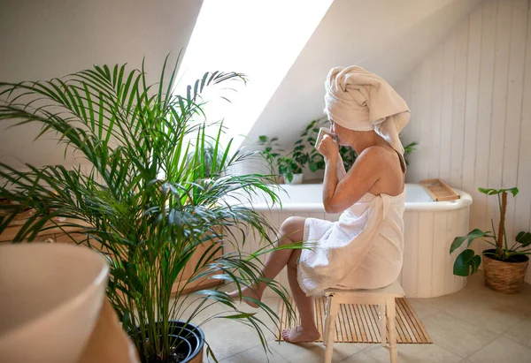 幸せな高齢者の女性は、自宅でバスルームにタオルで包まれ、コーヒーと休憩。. — ストック写真