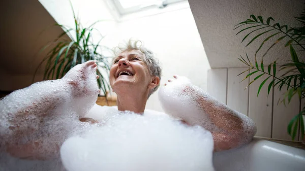 Fröhliche Seniorin wäscht sich zu Hause in Schaumbadewanne und lacht. — Stockfoto