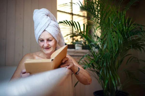 Wanita senior yang bahagia membaca buku di bak mandi di rumah. — Stok Foto