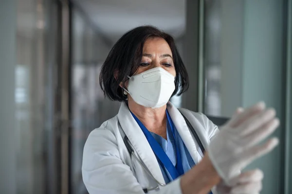 Portret van oudere vrouwelijke arts die handschoenen aantrekt in het ziekenhuis, coronavirus concept. — Stockfoto