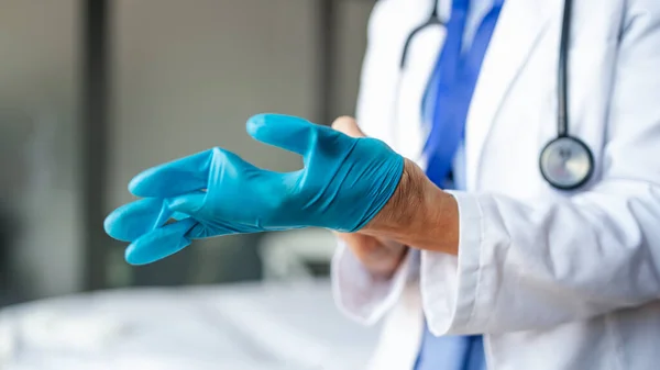 Médico senior irreconocible poniéndose guantes en el hospital, concepto de coronavirus. — Foto de Stock