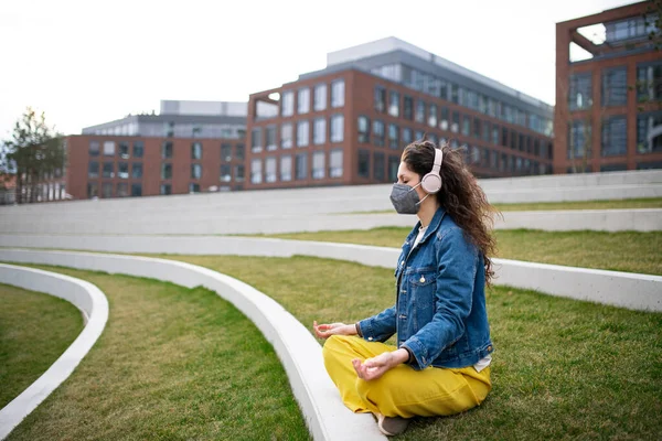 Kobieta ze słuchawkami uprawiająca jogę na świeżym powietrzu w parku w mieście, koncepcja koronawirusa. — Zdjęcie stockowe