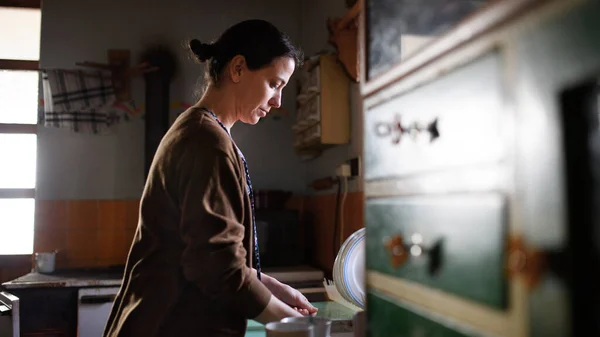 Poor mature woman washing dishes indoors at home, poverty concept. — Stock Photo, Image