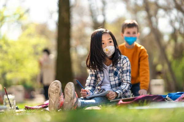 Маленькі діти, які сидять на відкритому повітрі в міському парку, навчаються груповій освіті та концепції коронавірусу . — стокове фото