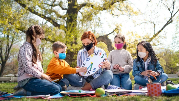 市内の公園で屋外に座っている小さな子供と教師,学習グループ教育とコロナウイルスの概念. — ストック写真