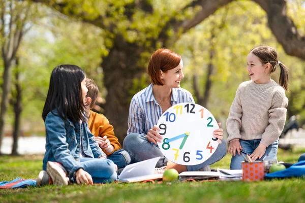 Teacher with small children sitting outdoors in city park, learning group education concept. — Stock Photo, Image