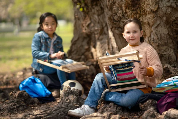 手の織機を持つ小さな子供たちは、都市公園で屋外に座って、グループ教育の概念を学ぶ. — ストック写真