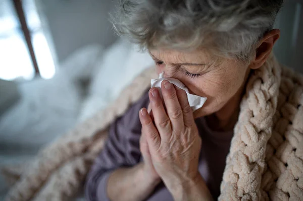 Zieke oudere vrouw in bed thuis, niezen en snuit neus. — Stockfoto