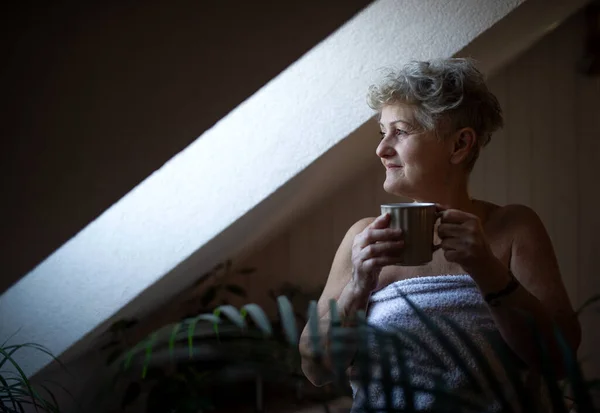 Mulher sênior feliz envolto em uma toalha no banheiro em casa, descansando com chá. — Fotografia de Stock