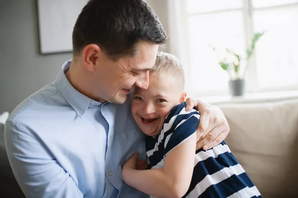 Vater mit glücklichem Down-Syndrom-Sohn zu Hause, umarmt und lacht. — Stockfoto