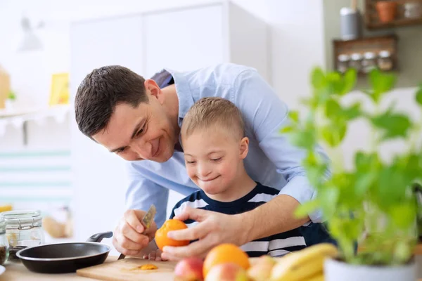 Pai com o filho de síndrome abaixo feliz em casa na cozinha, preparando a comida. — Fotografia de Stock