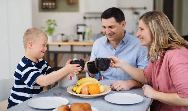 Família feliz com síndrome de down filho na mesa, tomando café da manhã. — Fotografia de Stock