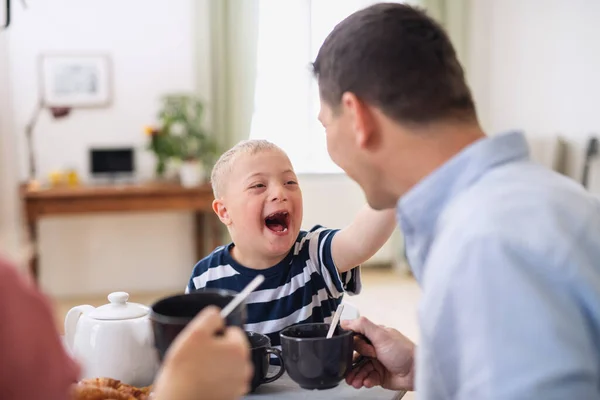 Lycklig familj med ner syndrom son vid bordet, skrattar när du äter frukost. — Stockfoto