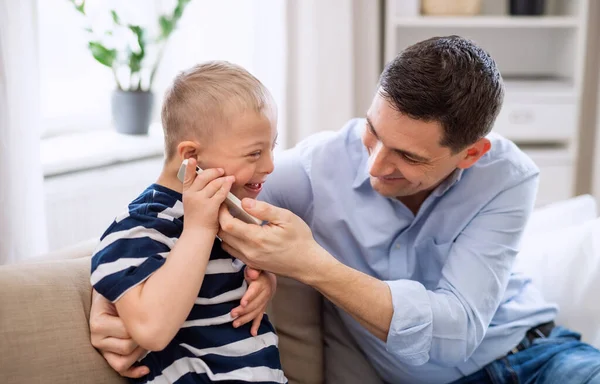 Vater mit glücklichem Down-Syndrom-Sohn zu Hause mit Smartphone. — Stockfoto