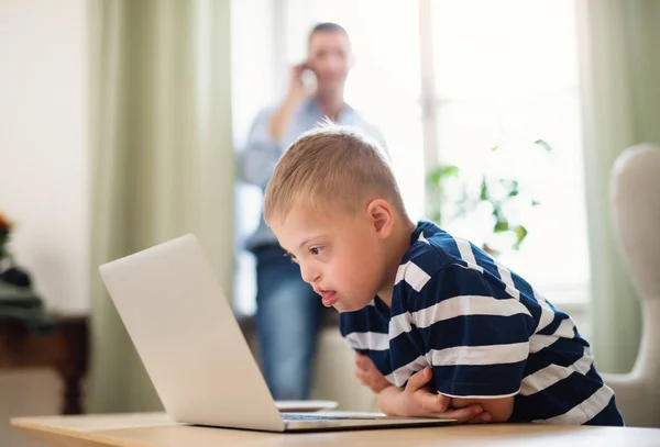 Down syndrom pojke med oigenkännlig far inomhus, med hjälp av laptop. — Stockfoto