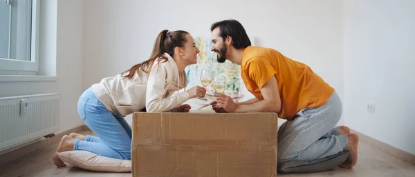 Pareja joven con cajas y vino moviéndose en nuevo piso, nuevo hogar y concepto de reubicación. — Foto de Stock