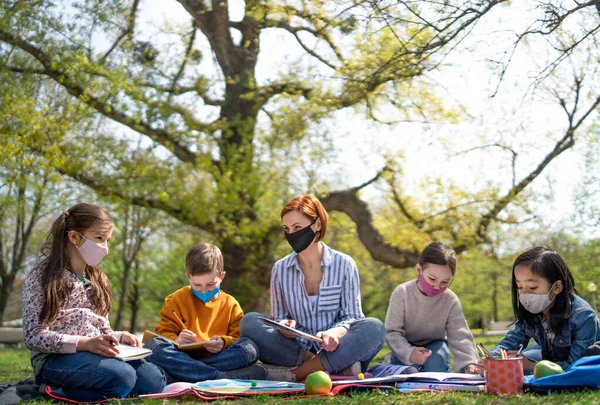 Profesor con niños pequeños sentado al aire libre en el parque de la ciudad, aprendizaje de la educación en grupo y el concepto coronavirus. — Foto de Stock