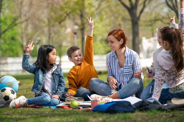 Učitel s malými dětmi sedící venku v městském parku, koncepce skupinového vzdělávání. — Stock fotografie