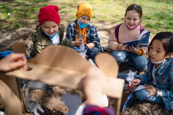 Преподаватель с маленькими детьми, сидящий на открытом воздухе в городском парке, обучение группового образования и концепции коронавируса. — стоковое фото