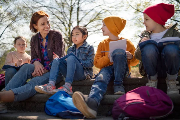 Insegnante con bambini piccoli seduto all'aperto nel parco cittadino, concetto di istruzione di gruppo di apprendimento. — Foto Stock