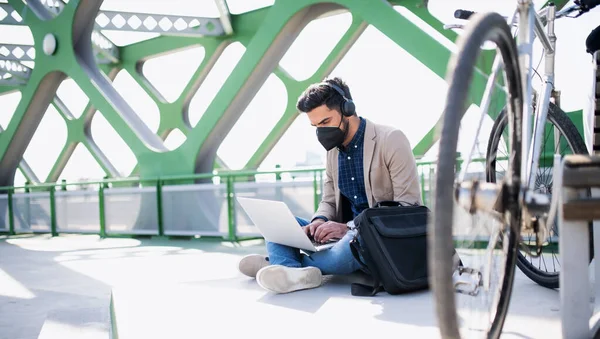 Młody biznesmen dojeżdżający z laptopem pracujący na drodze do pracy na świeżym powietrzu na moście w mieście, koncepcja koronawirusa. — Zdjęcie stockowe