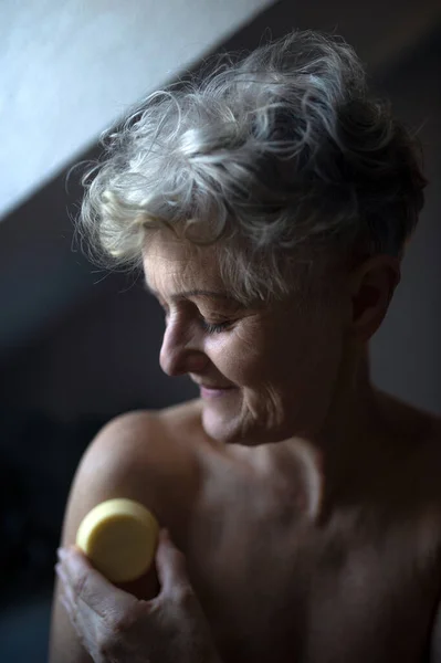 Feliz mujer mayor en topless en el baño en casa, utilizando cubo de masaje. —  Fotos de Stock