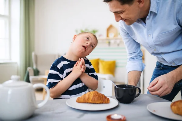 Down menino síndrome com o pai na mesa, tomando café da manhã. — Fotografia de Stock