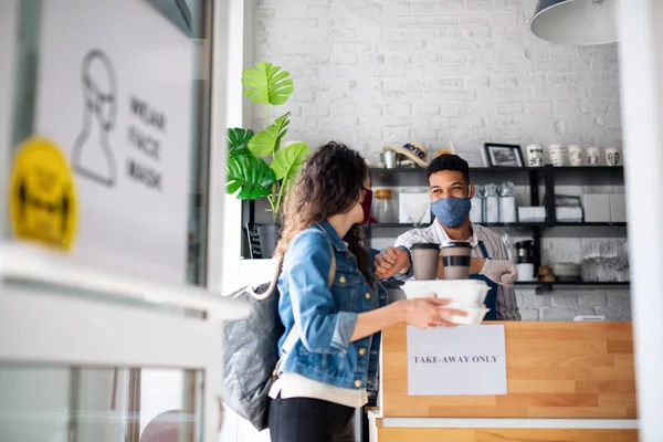 Frau mit verpacktem Essen und Kaffee zum Mitnehmen, grüßt Kellnerin im Café. Coronavirus-Konzept. — Stockfoto