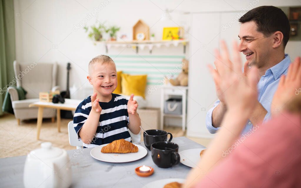 Happy family with down syndrome son at the table, clapping when having breakfast.