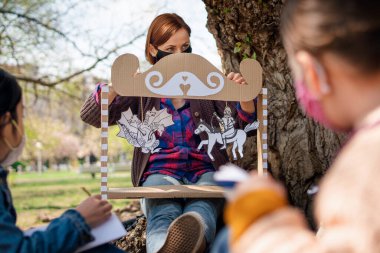 Küçük çocuklu öğretmen şehir parkında oturuyor, grup eğitimi ve koronavirüs konseptini öğreniyor..