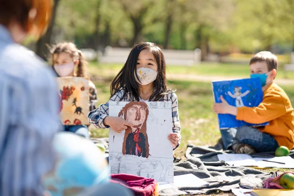 Маленькие дети с учителем на открытом воздухе в городском парке, обучение групповое образование и коронавирусная концепция. — стоковое фото