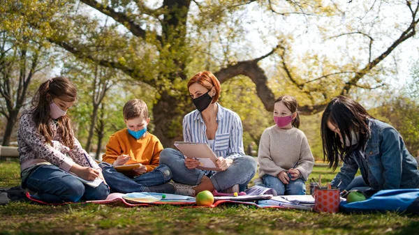 Nauczyciel z małymi dziećmi siedzącymi na świeżym powietrzu w parku miejskim, edukacja grupowa i koncepcja koronawirusa. — Zdjęcie stockowe