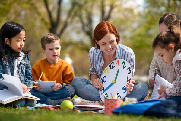 Вчителька з маленькими дітьми, сидячи на відкритому повітрі в міському парку, концепція групової освіти . — стокове фото