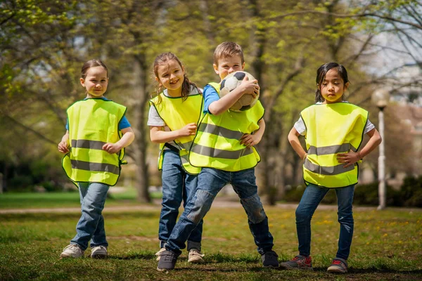 Niños pequeños con pelota mirando a la cámara al aire libre en el parque de la ciudad, aprendiendo el concepto de educación en grupo. — Foto de Stock