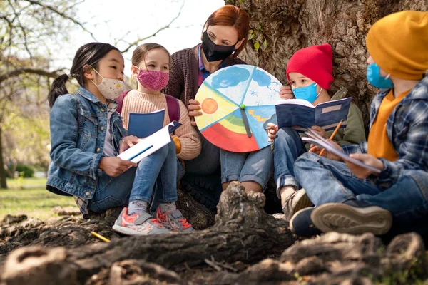 Преподаватель с маленькими детьми, сидящий на открытом воздухе в городском парке, обучение группового образования и концепции коронавируса. — стоковое фото